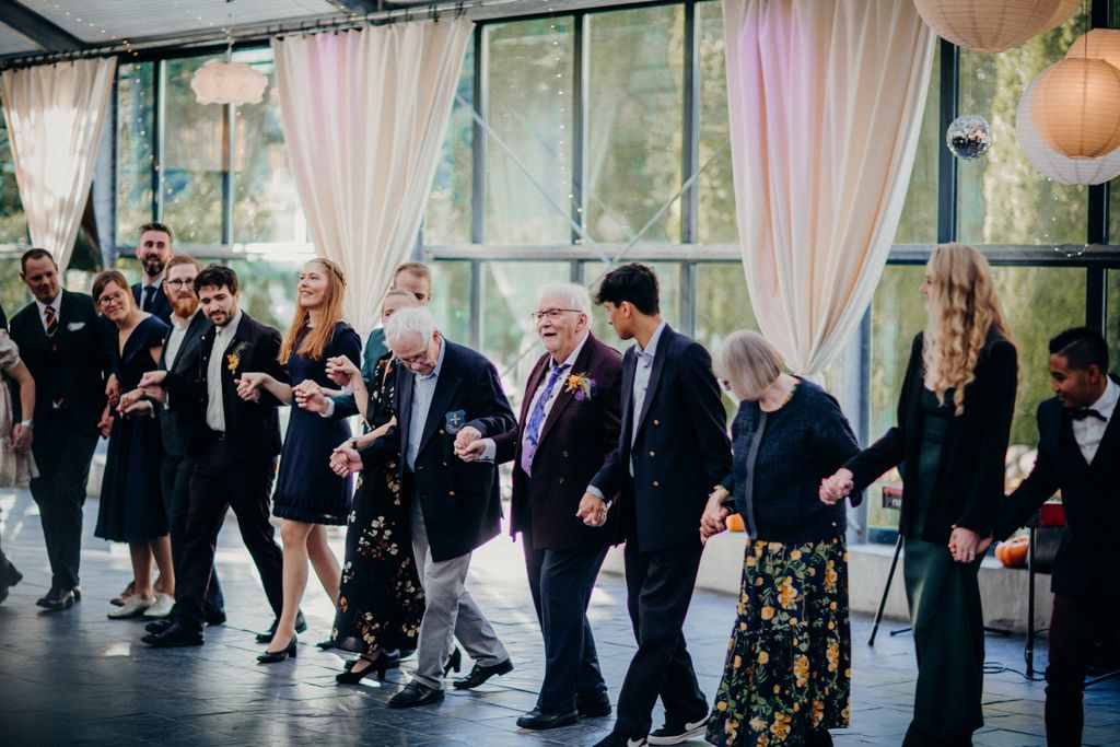 A diverse group of people joyfully dancing and holding hands indoors at a celebration.