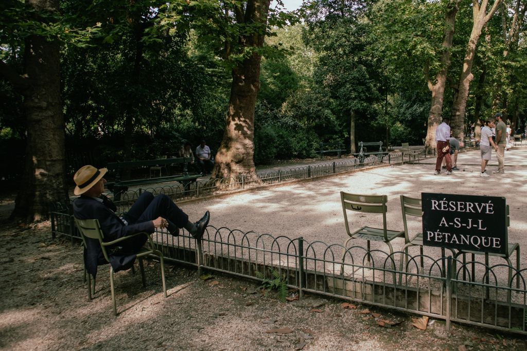 A serene park scene in Paris with a man relaxing, people playing pétanque.
