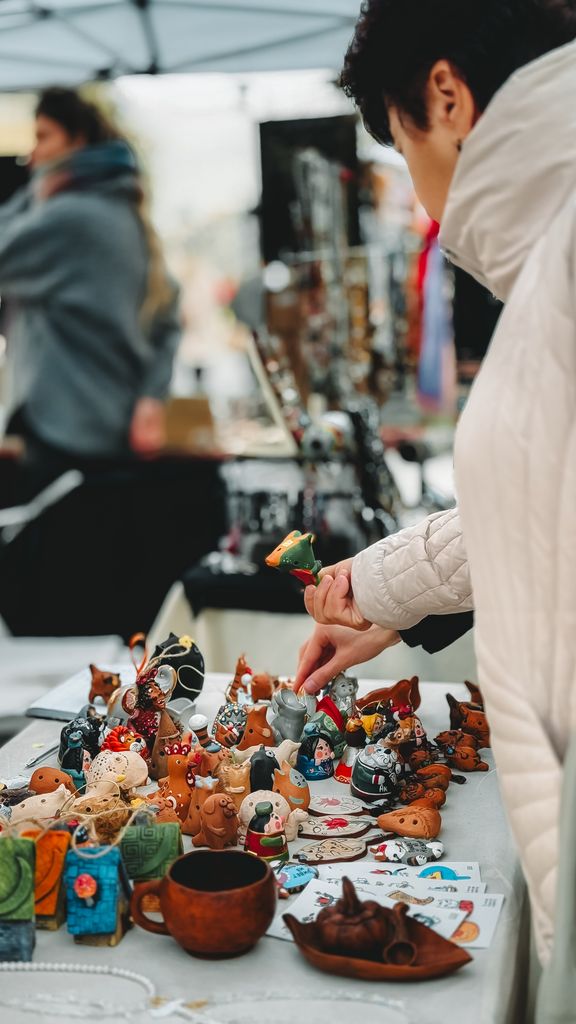 Adult browsing handmade animal sculptures at outdoor craft market.