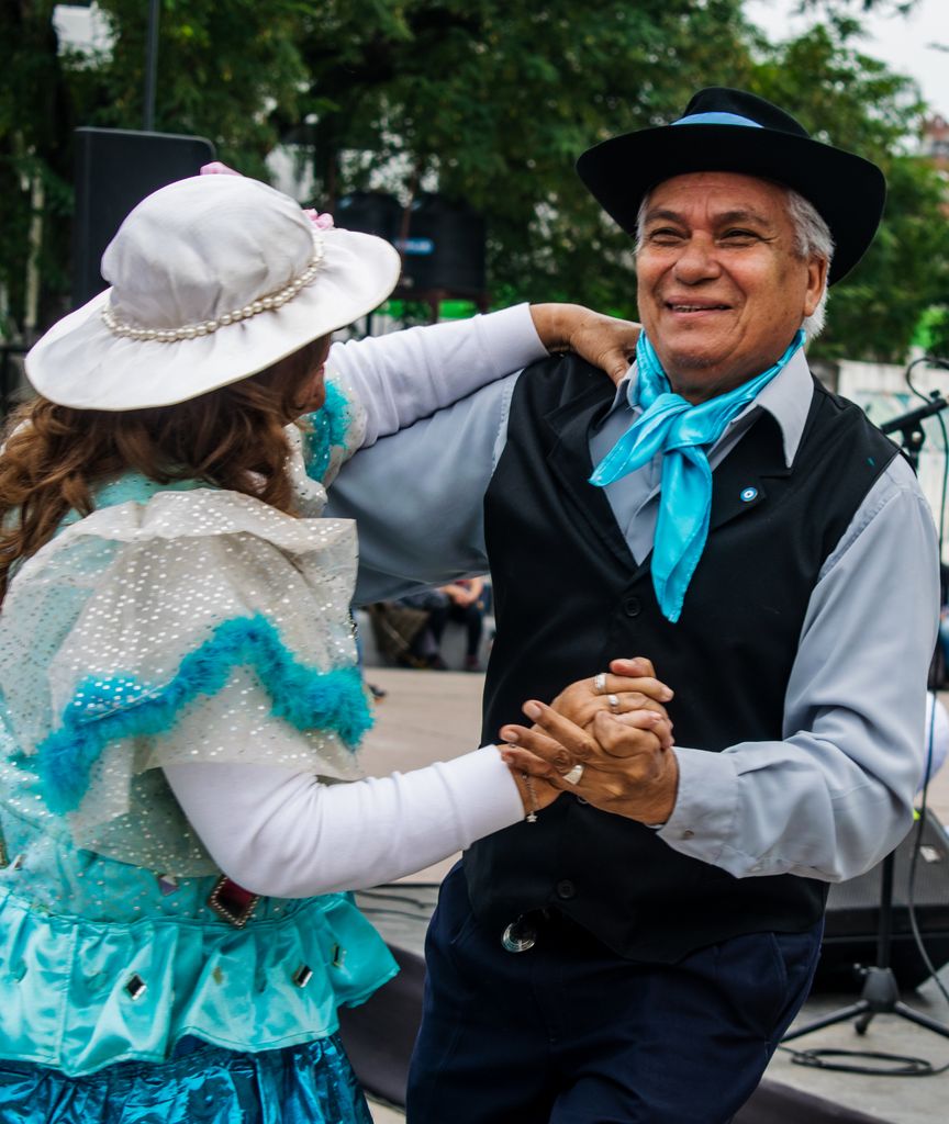 Elderly couple joyfully dancing traditional Argentine dance outdoors.