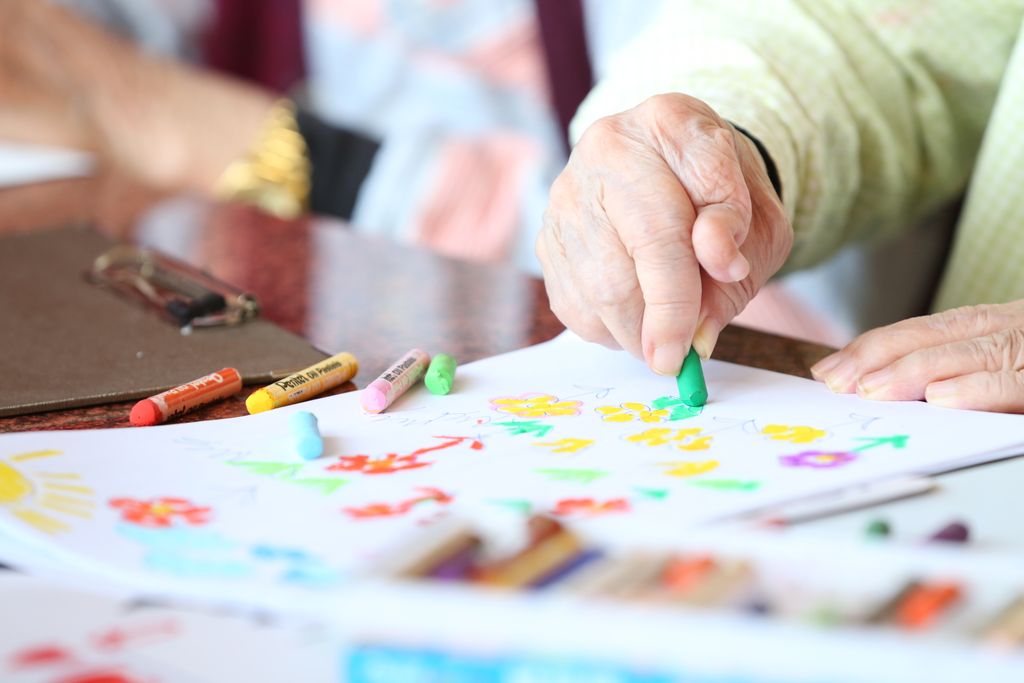 Faceless elderly person with rheumatoid arthritis drawing with crayon during rehabilitation in nursing home