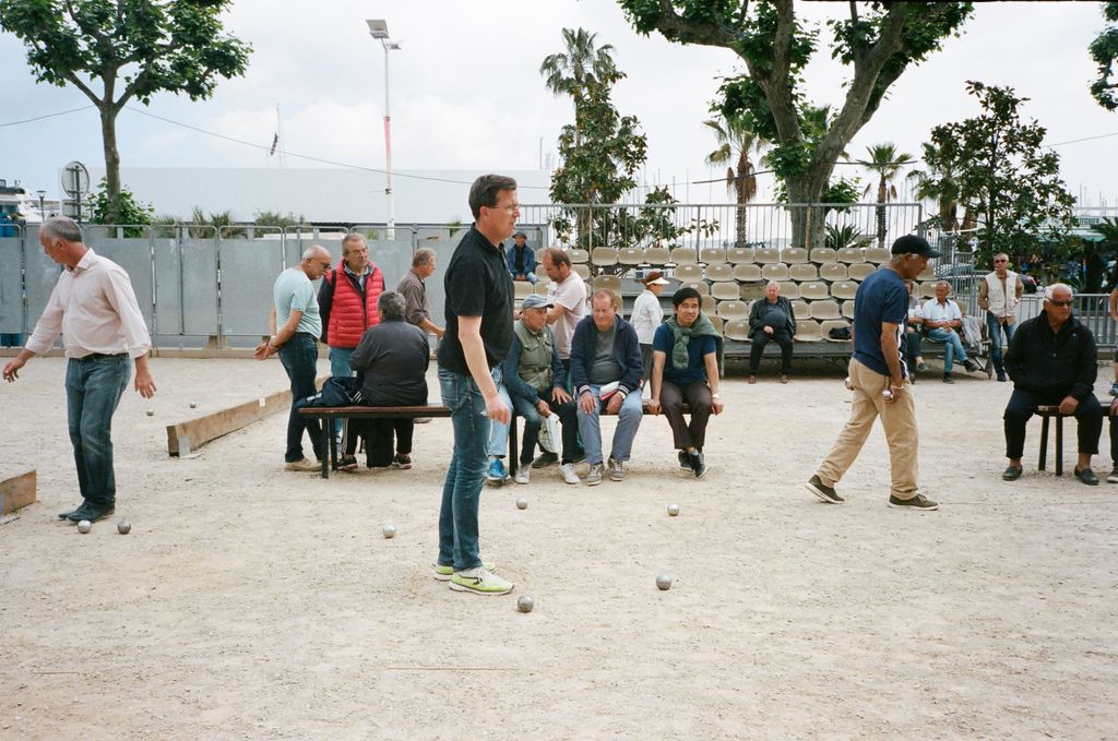 Group of diverse male players on sports ground playing petanque game with small balls and benches in town