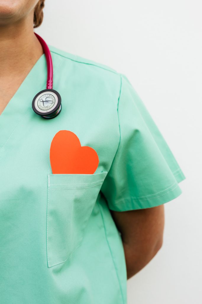 Nurse in pastel green scrubs with stethoscope and paper heart for heart health awareness.