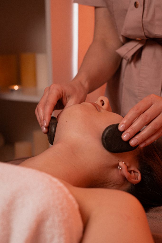 Relaxing stone massage on woman's face in a calm spa environment.