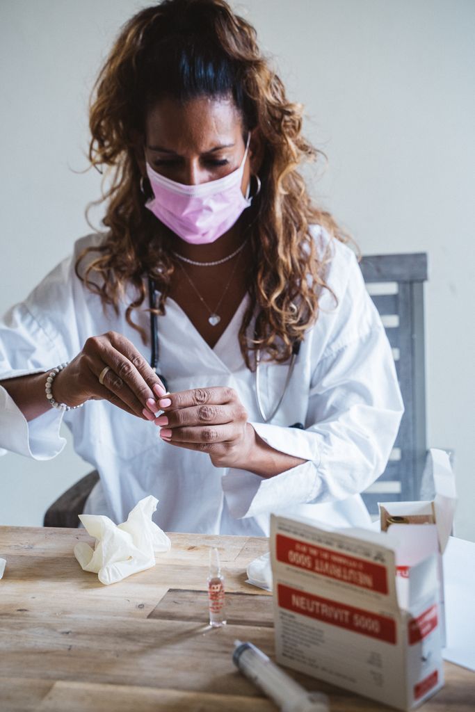 Woman doctor in a face mask preparing a syringe for vaccination indoors.